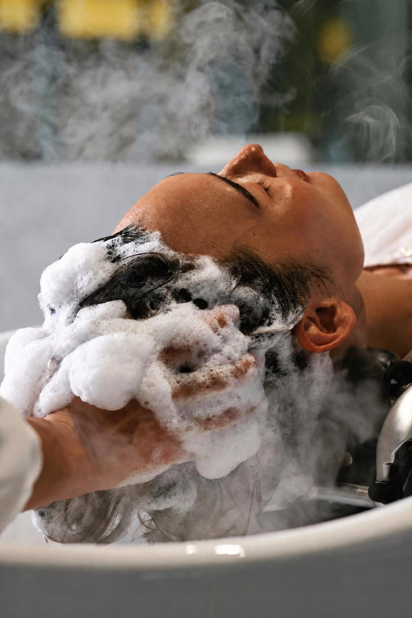 Cliente allongée pendant un Japanese Head Spa, le cuir chevelu couvert de mousse dans la brume