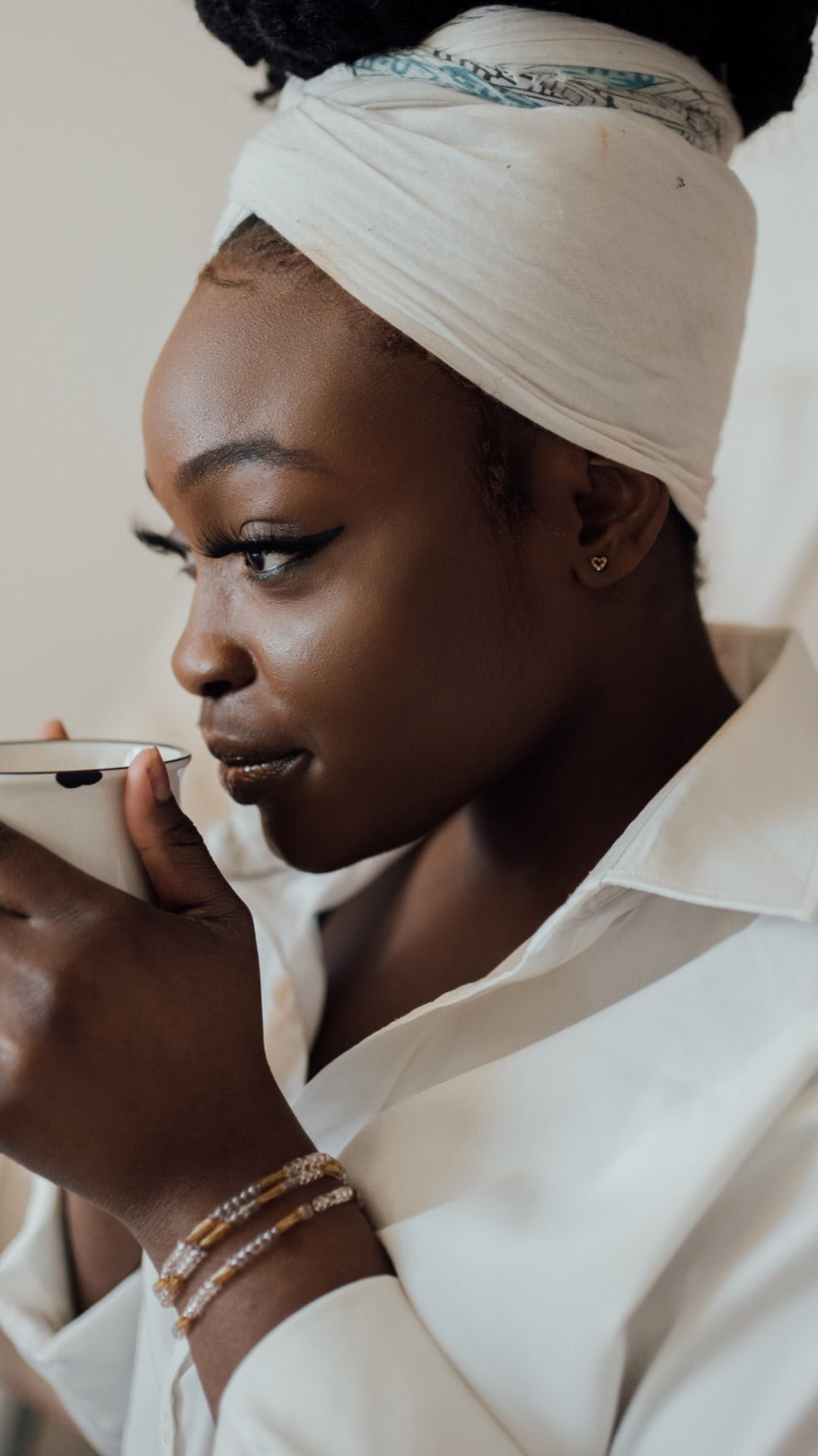 Femme de profil, un foulard clair noué sur les cheveux, une tasse à la main