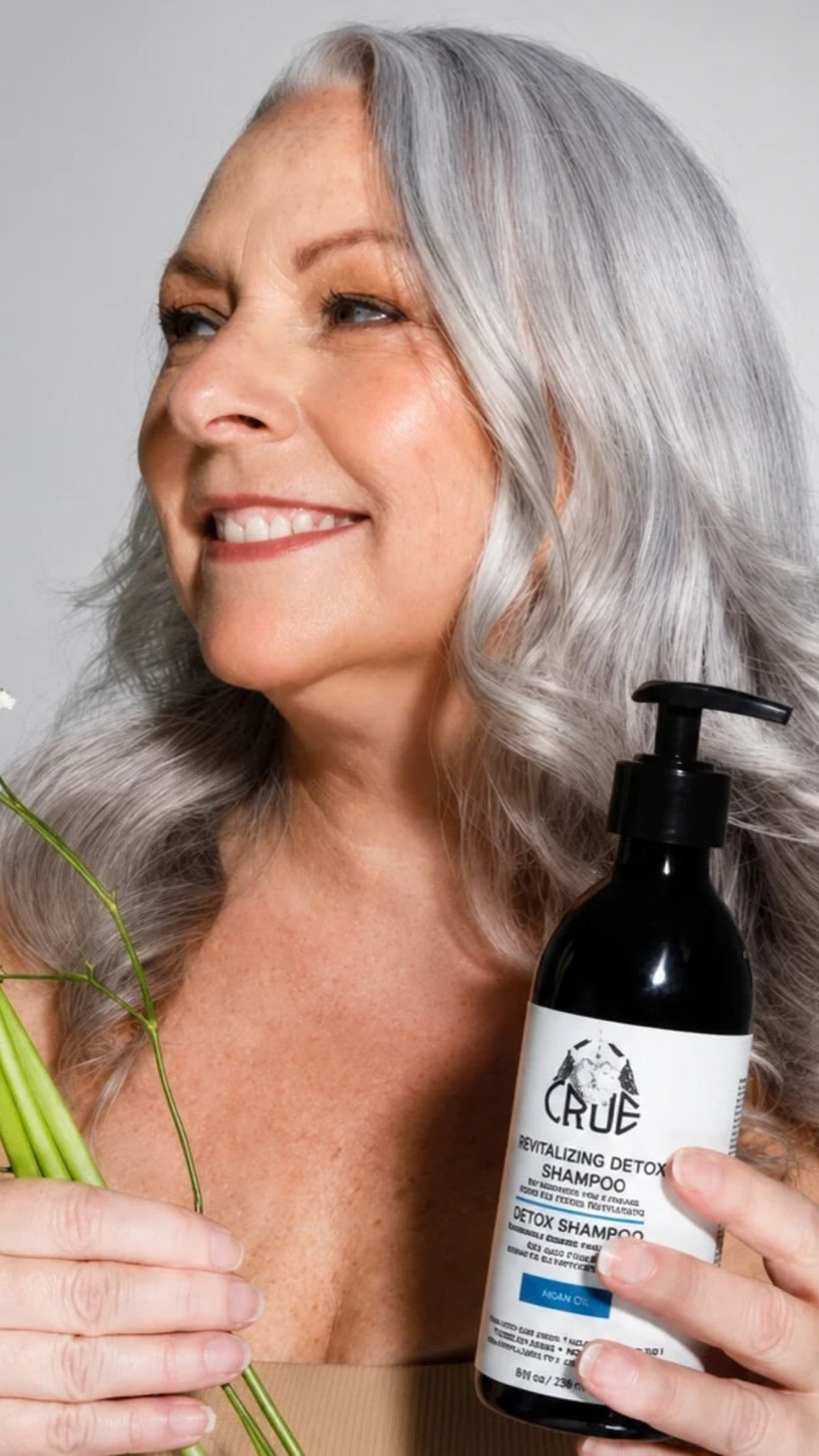 Cliente souriante aux longs cheveux gris, un shampoing CRÜE à la main